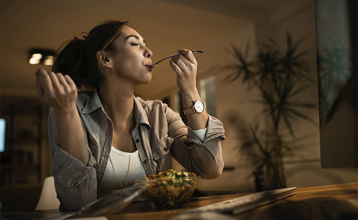Mulher comendo salada com os olhos fechados.