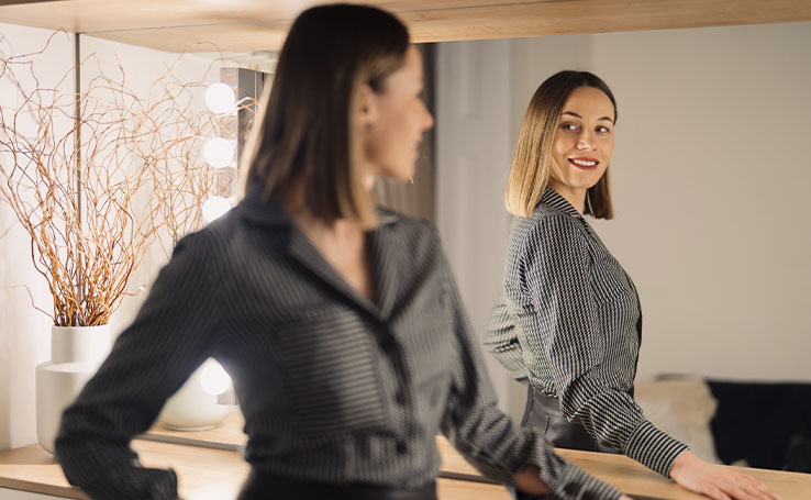 mulher se olhando no espelho com uma postura de quem tem boa autoestima, um importante passo para desenvolver a inteligência emocional