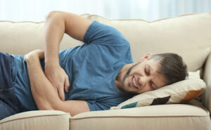homem deitado no sofá com a mão sobre a barriga, pois está com dores causadas pos gases intestinais