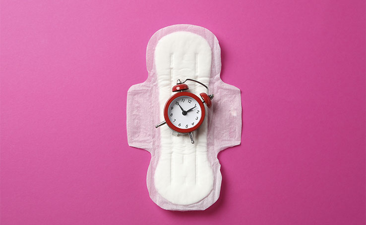 relógio em cima de absorvente indicando atraso na menstruação