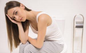 mulher sentada no vaso sanitário com semblante de dor, pois está com constipação intestinal